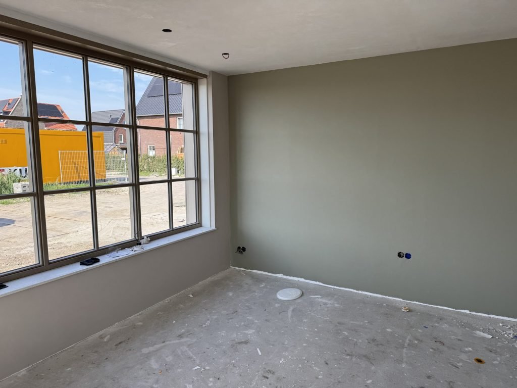 Nieuwbouwkamer met een groot raam met roedes en een egale wand in grijsgroen
