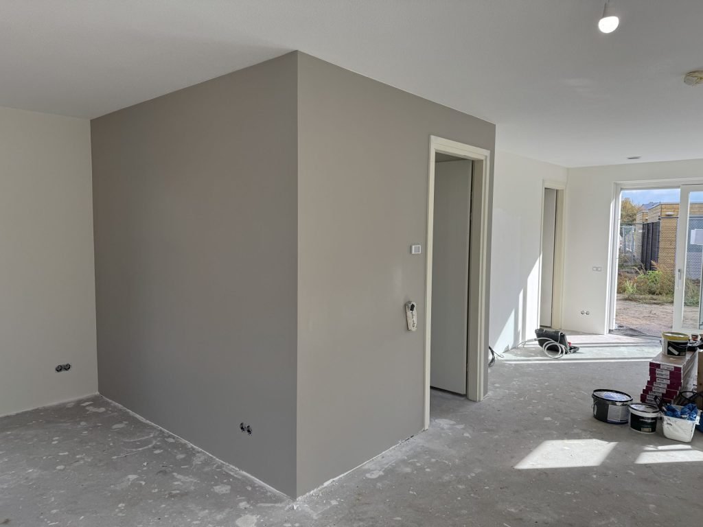 Grijs geverfde vlieswand rond de meterkast in een nieuwbouwwoning, met verfemmers op de vloer