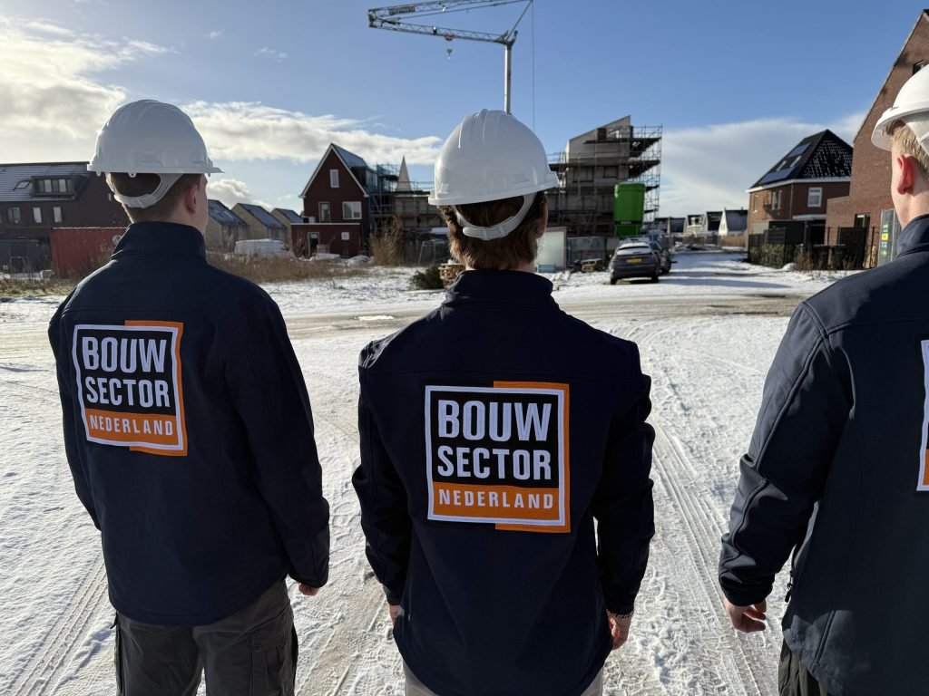 Drie medewerkers van Bouwsector Nederland met witte helm op een besneeuwd nieuwbouwterrein met een bouwkraan